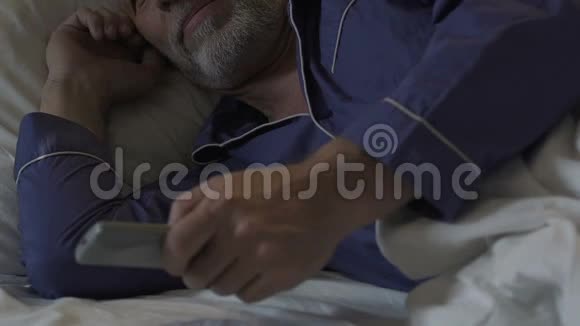 老年男性晚上躺着睡不着觉用遥控器切换电视频道视频的预览图