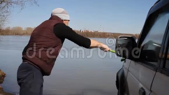 一个男人用拖把和一块抹布从河上的桶里洗一辆越野车视频的预览图