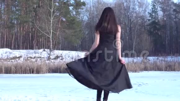 一个年轻的微笑着的黑发女孩穿着黑色的衣服转过身把手放在冬天的森林景观背景上视频的预览图