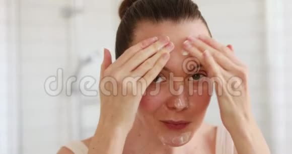 女人在镜子里的脸上涂抹保湿霜视频的预览图