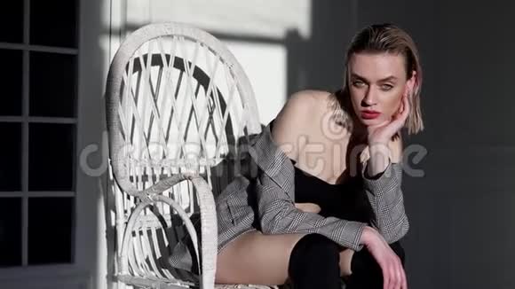 穿夹克的时髦女人坐在房间里的白色扶手椅里视频的预览图