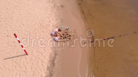 妈妈和女儿正在海滩上玩耍建造一座沙堡夏日阳光明媚假期空中射击视频的预览图