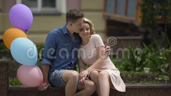 一个拿着气球拥抱女友的男人亲吻她的脸颊拥抱她视频的预览图