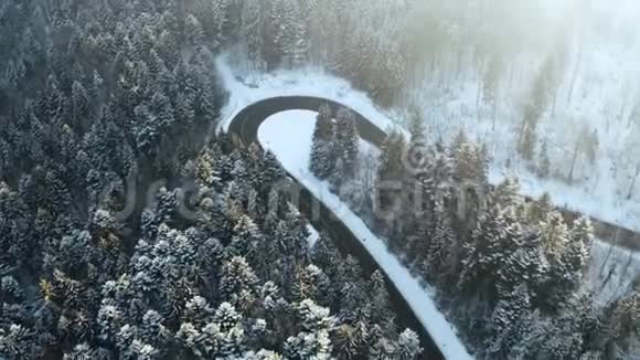 头顶高空俯视汽车行驶在簪弯转弯的山路上冬雪覆盖森林白色视频的预览图