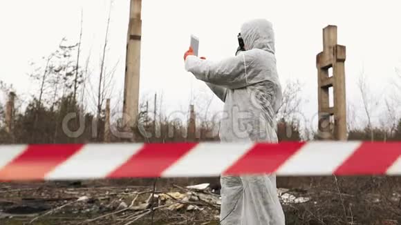 穿着生物危害套装和防毒面具的男人在智能手机上拍照视频的预览图