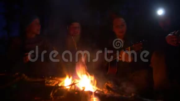 晚上在树林里的篝火旁欢快的年轻人唱着歌弹着吉他视频的预览图