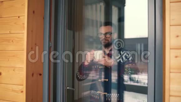 男人在窗边喝茶或喝咖啡透过玻璃看视频的预览图