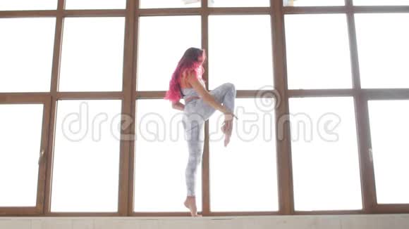 拉伸和柔韧性的概念穿着运动服的年轻女子在白色的室内靠近窗户伸展身体视频的预览图