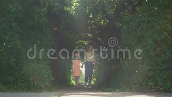 金发母亲和女儿一起在夏天的花园或公园里牵手散步家庭幸福与自然的联系视频的预览图