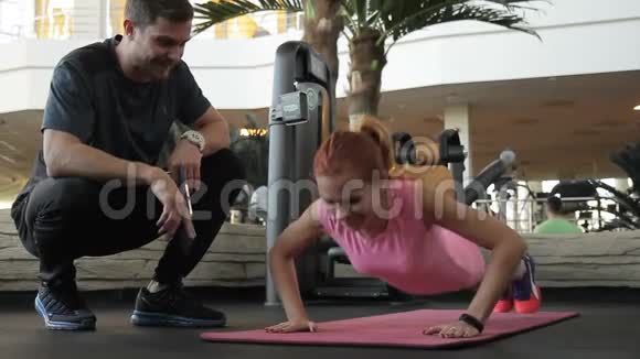 在教练的监督下一个健身俱乐部里的女人扭动着她的手臂视频的预览图