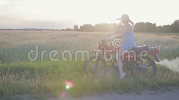 一位戴着帽子的年轻女士骑着一辆复古摩托车在田野和草地之间的土路上享受着乐趣视频的预览图