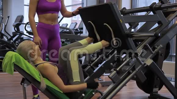 女教练正在教年轻的女运动员如何在健身房做腿部按压视频的预览图