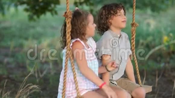 一个女孩和一个男孩在校学生哥哥和姐姐正坐在公园的秋千上热情地交谈着视频的预览图