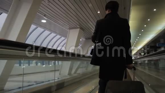 一个穿着黑色外套带着手提箱的人正在乘坐机场自动扶梯返回视频的预览图