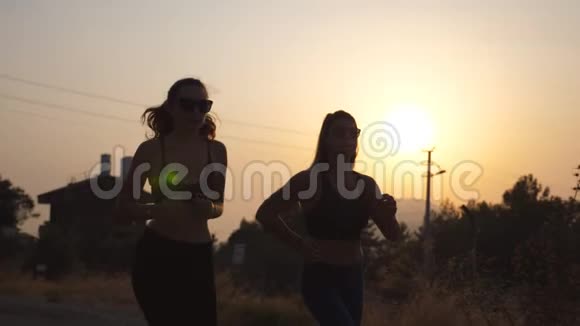 日落时分两个年轻女孩在户外跑步年轻的运动女性在乡间路慢跑女运动员训练视频的预览图