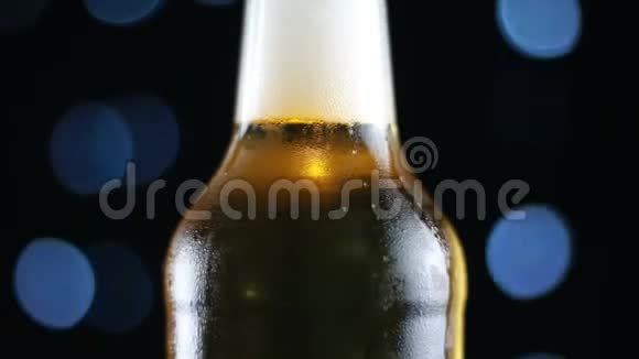 开着明亮的灯在黑色背景上旋转的透明瓶子里的冷啤酒视频的预览图