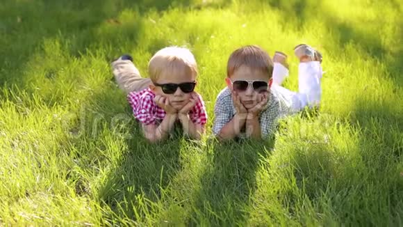 夏天两个快乐的小男孩戴着太阳镜躺在草地上肖像视频的预览图