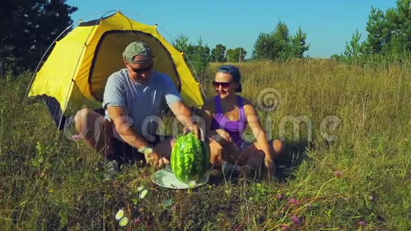 幸福的男人和女人在森林里的帐篷附近人用刀切西瓜视频的预览图