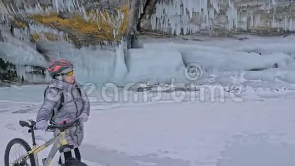 女人正走在冰窟附近的自行车旁有冰洞和冰柱的岩石非常美丽女孩是视频的预览图