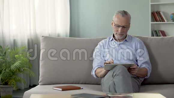 微笑的老人坐在沙发上看女儿的平板照片视频的预览图