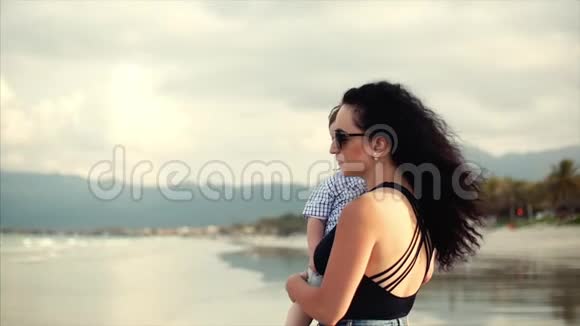 年轻的家庭一个母亲抱着一个儿子一个幸福的家庭沿着海滨散步视频的预览图