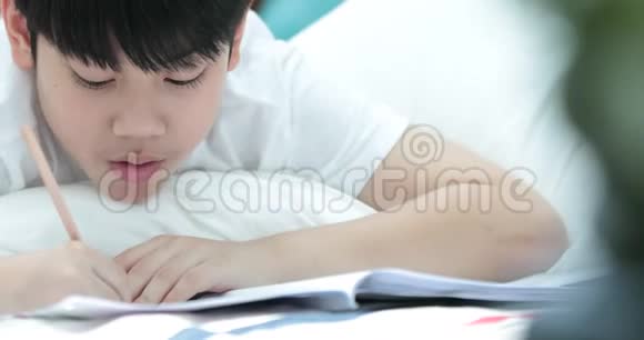 快乐的亚洲可爱男孩手拿铅笔在家写作业视频的预览图