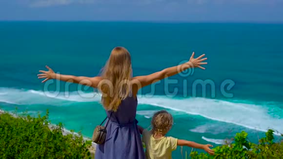 一个年轻的女人和她的儿子站在悬崖边看着海洋的慢镜头苏鲁班和恩阳视频的预览图