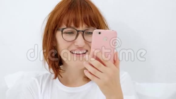 一个带着手机的女孩的肖像在智能手机中找到你最喜欢的曲调微笑着通过耳机听它视频的预览图
