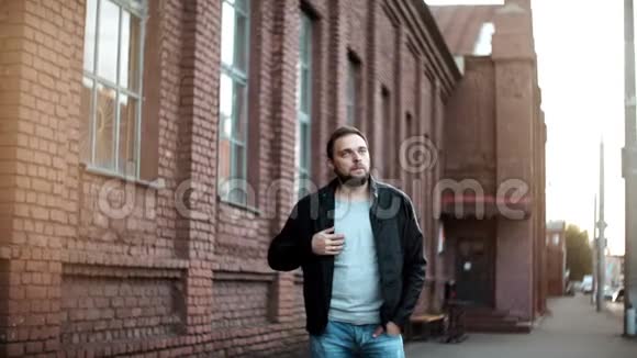 中等镜头的休闲欧洲男子肖像穿着皮夹克的年轻男子正在等待红砖楼4K视频的预览图