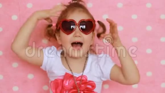 可爱的小女孩时尚主义者微笑笑露出舌头粉色背景有趣的孩子穿着红色太阳镜视频的预览图