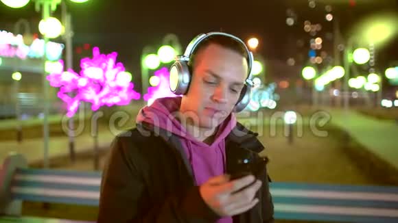 笑容可掬帅哥戴着无线黑色耳机从智能手机里听音乐翩翩起舞视频的预览图