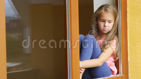 伤心的女孩在家透过窗户看着视频的预览图