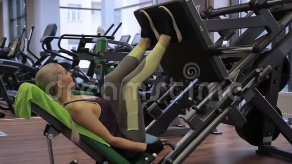 这位金发女人正在明亮的健身房里用现代设备做腿部按压视频的预览图