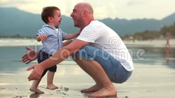 年轻的家庭父亲和儿子一个快乐的儿子拥抱他的父亲在海岸幸福的家庭沿着海岸散步视频的预览图