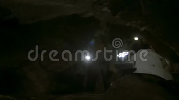 手持手电筒的头盔在洞穴学家面前探索黑暗狭窄的洞穴视频的预览图