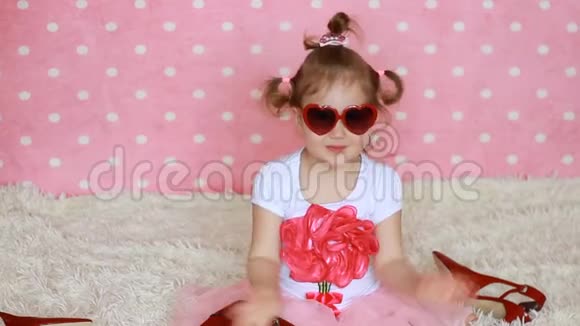 可爱的小女孩戴着红色太阳镜以心形的形式发送空气亲吻有趣的孩子送吻粉色背景视频的预览图