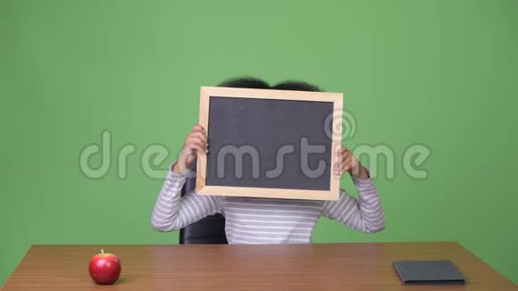 年轻可爱的非洲女孩一头非洲头发坐在黑板上视频的预览图