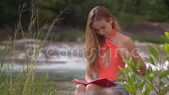 穿着亮橙色上衣的女孩和书和河视频的预览图