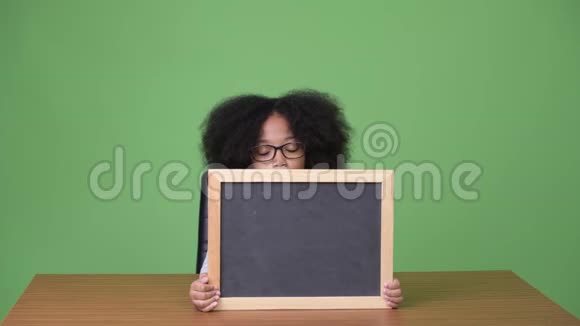 年轻可爱的非洲女孩一头非洲头发坐在黑板上视频的预览图