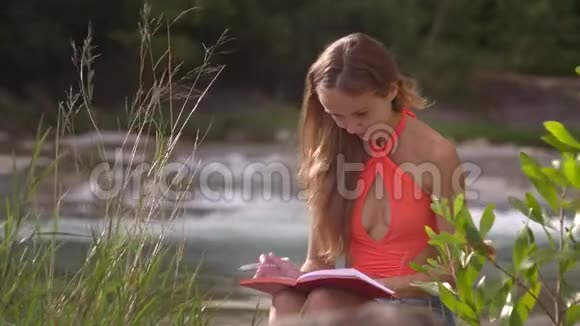橙色上衣的女孩在河流中作笔记视频的预览图