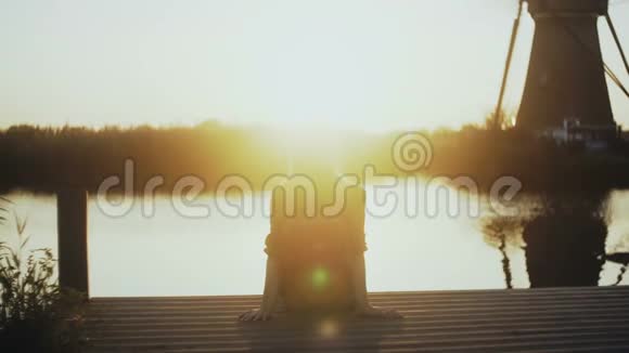 女人坐在一个小湖码头上看日落黄金时间完美的平静和内心和谐的时刻4K后视图视频的预览图
