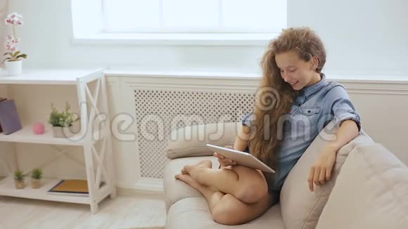 漂亮的少女在沙发上用平板电脑放松使用平板电脑和平板电脑在沙发上放松的一个可爱女孩的照片视频的预览图