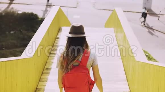 长发女子走在城市桥上带红色背包的欧洲女孩黄色城市走道墙4K视频的预览图