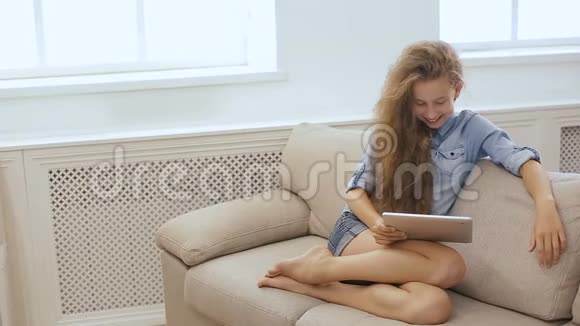 漂亮的少女在沙发上用平板电脑放松使用平板电脑和平板电脑在沙发上放松的一个可爱女孩的照片视频的预览图