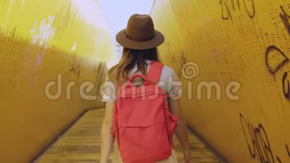 戴着红色背包的女孩走在黄色的隧道里女人走在艺术安装桥墙之间鹿特丹4K视频的预览图