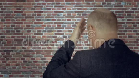 成年男子在砖墙背景下用手敲前额后景视频的预览图