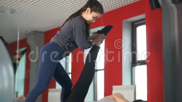 女私人教练在窗边帮助年轻人做伸展运动视频的预览图