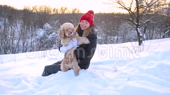 在户外雪地里和她的狗坐在一起的年轻女人视频的预览图