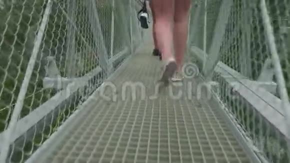 镜头跟随两位年轻的运动白种人妇女在高山上的吊桥上行走视频的预览图