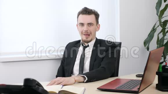 穿西装的年轻商人坐在办公室里伸着舌头使滑稽的脸60英尺长视频的预览图